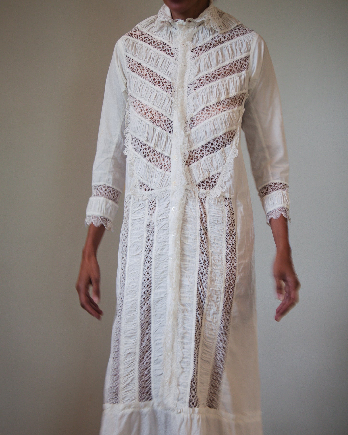 A long white embroidered nightgown with sheer lace panels and detailing, shown on a woman against a plain light gray background.