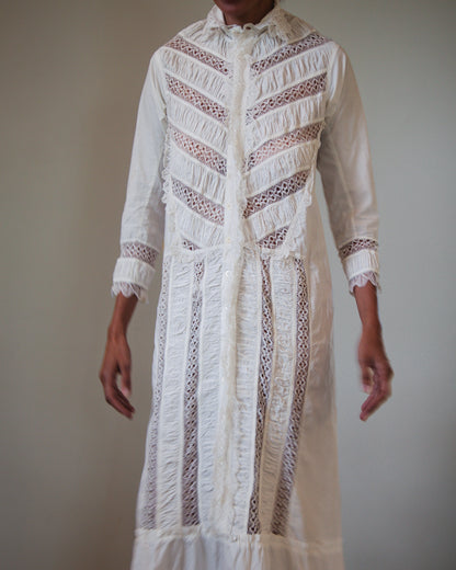 A long white embroidered nightgown with sheer lace panels and detailing, shown on a woman against a plain light gray background.