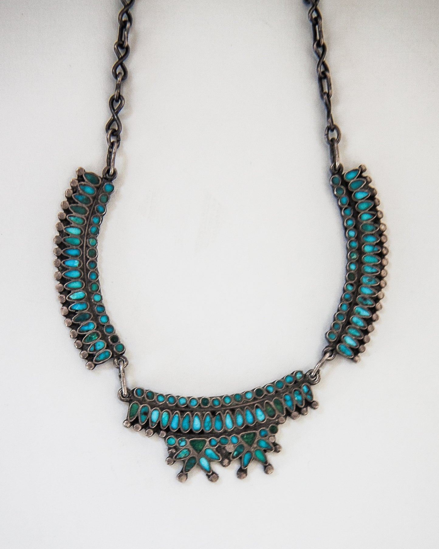 A silver-toned statement necklace featuring multiple rows of small turquoise-colored stones, displayed against a plain white background.