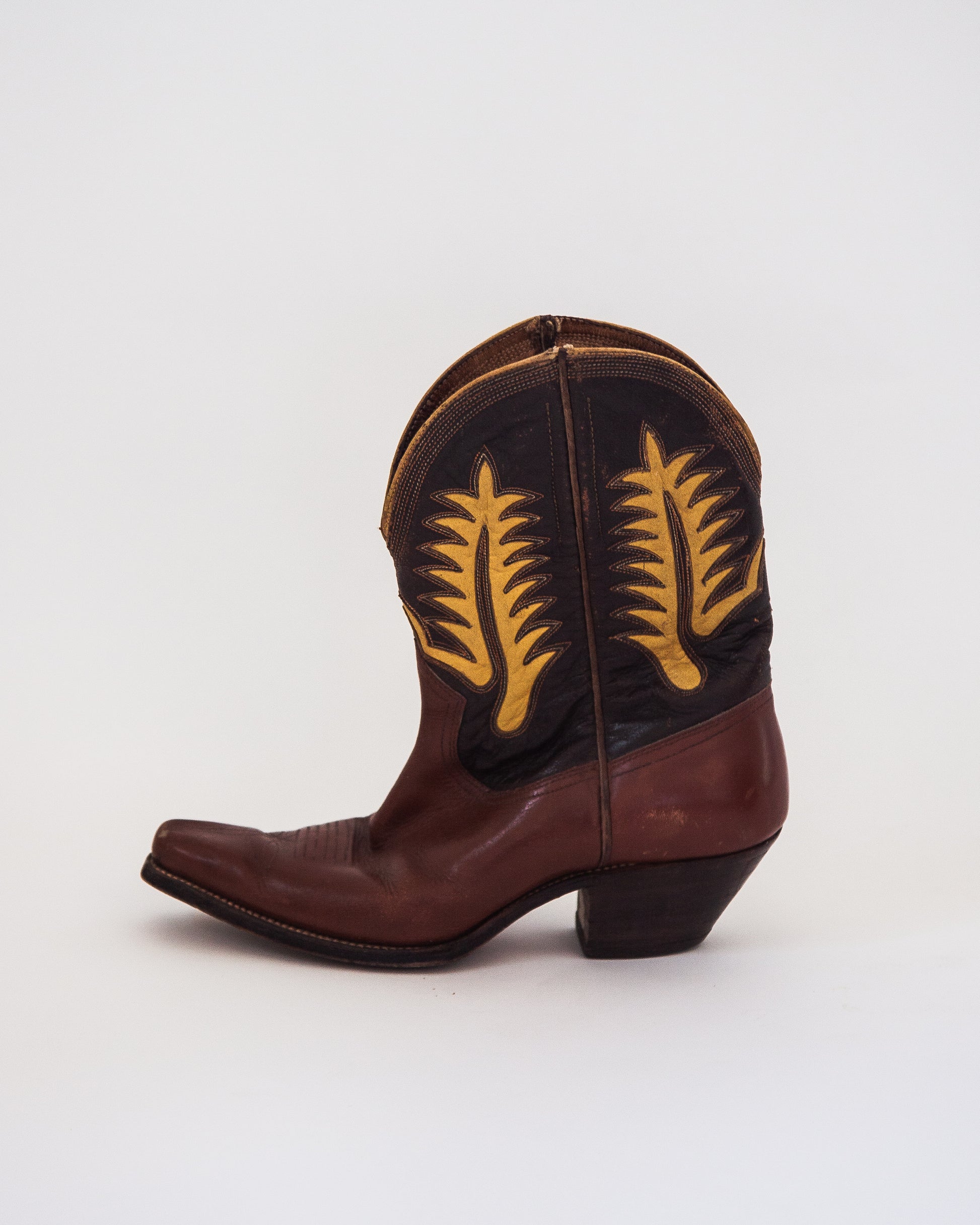 A single brown leather cowboy boot with yellow embroidered feather designs, shown from a side profile on a light gray background.