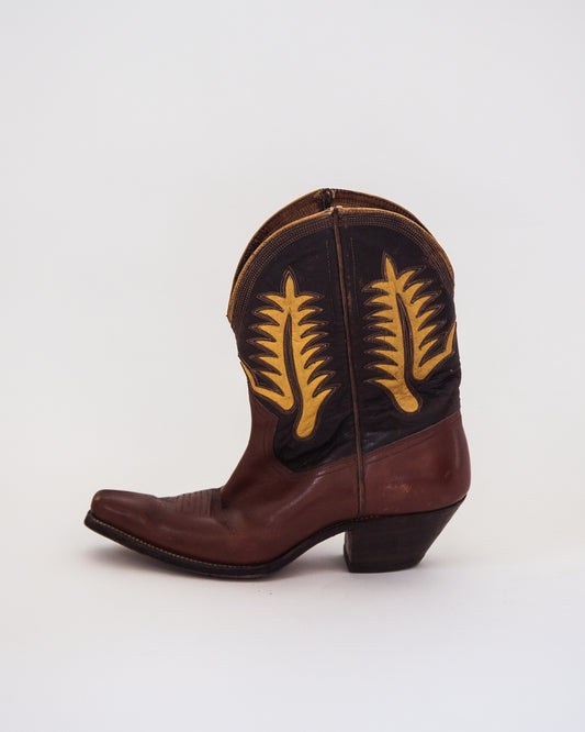A single brown leather cowboy boot with yellow embroidered feather designs, shown from a side profile on a light gray background.