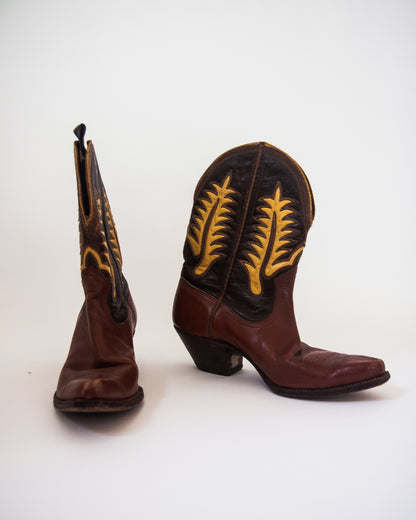 A pair of brown leather cowboy boots with yellow embroidered leaf patterns on the shafts, shown against a plain white background.