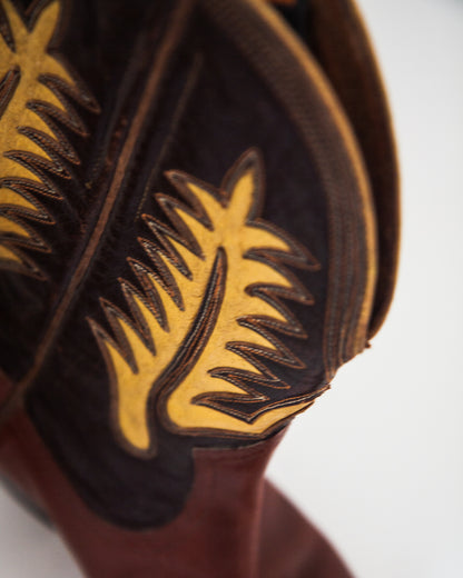 Close-up of a western boot showing dark brown leather with yellow embroidered decorative stitching on a white background.