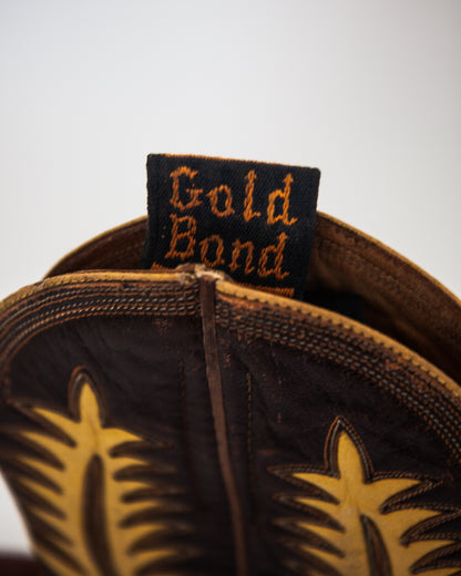 Close-up of the inside tab of a brown leather cowboy boot with tan western-style stitching and a fabric brand tag reading Gold Bond.