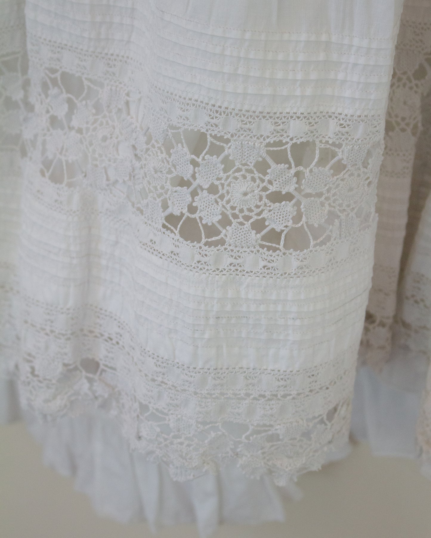 Close-up of a white cotton garment with intricate floral lace trim and ruffled edges.