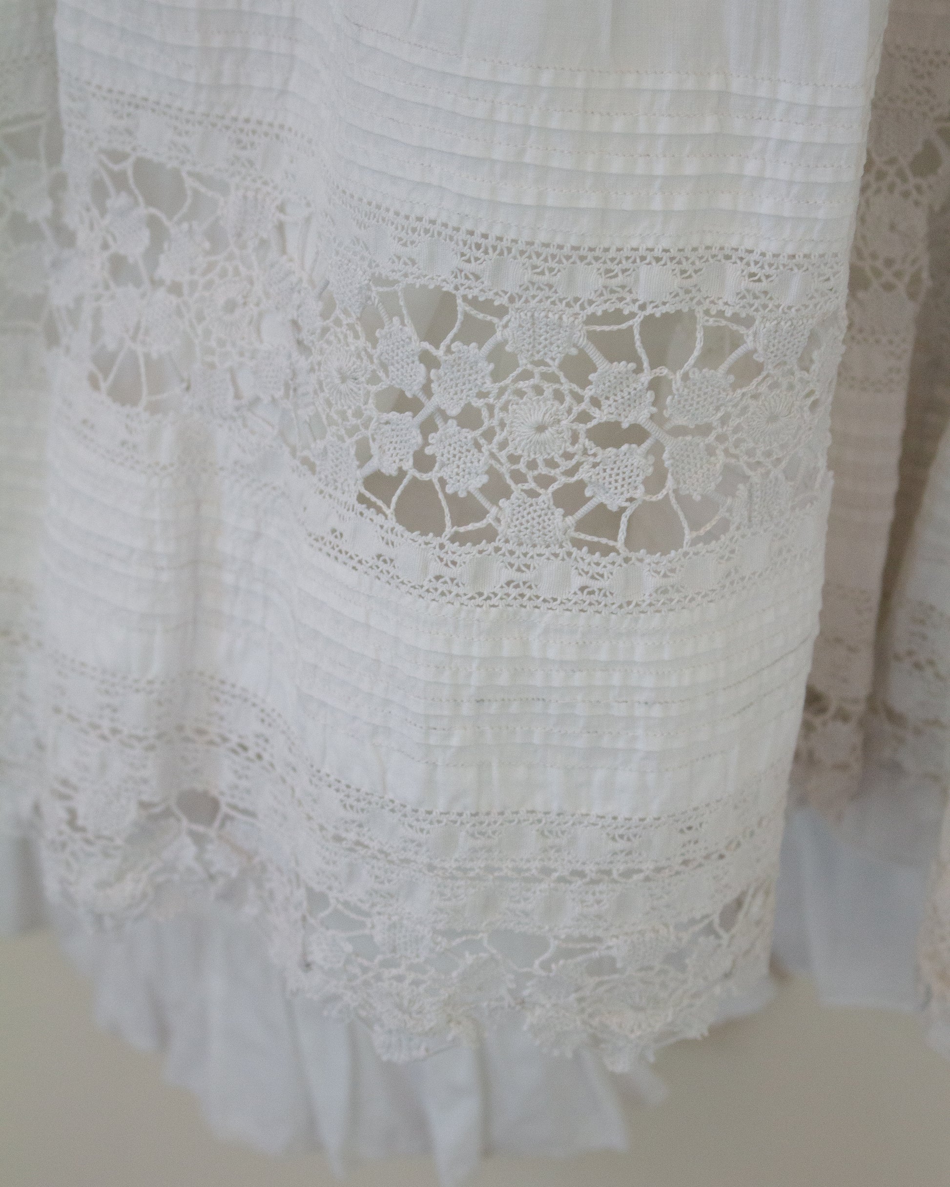 Close-up of a white cotton garment with intricate floral lace trim and ruffled edges.
