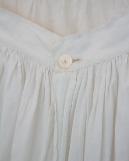 Close-up detail of a white pleated fabric garment, showing gathered seams and a single round button at the waistband.