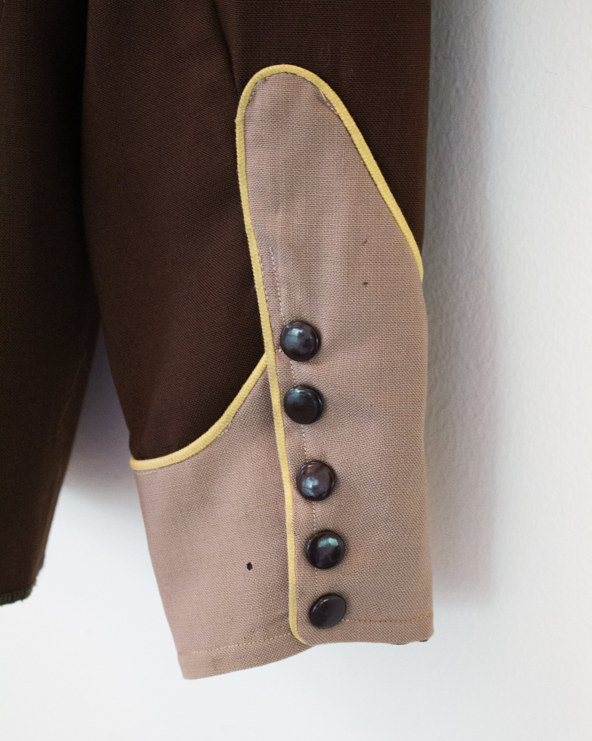 Close up of the sleeve of a brown and tan shirt with yellow trim with a broken button