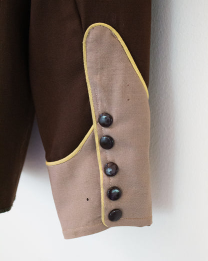 Close up of the sleeve of a brown and tan shirt with yellow trim with a broken button