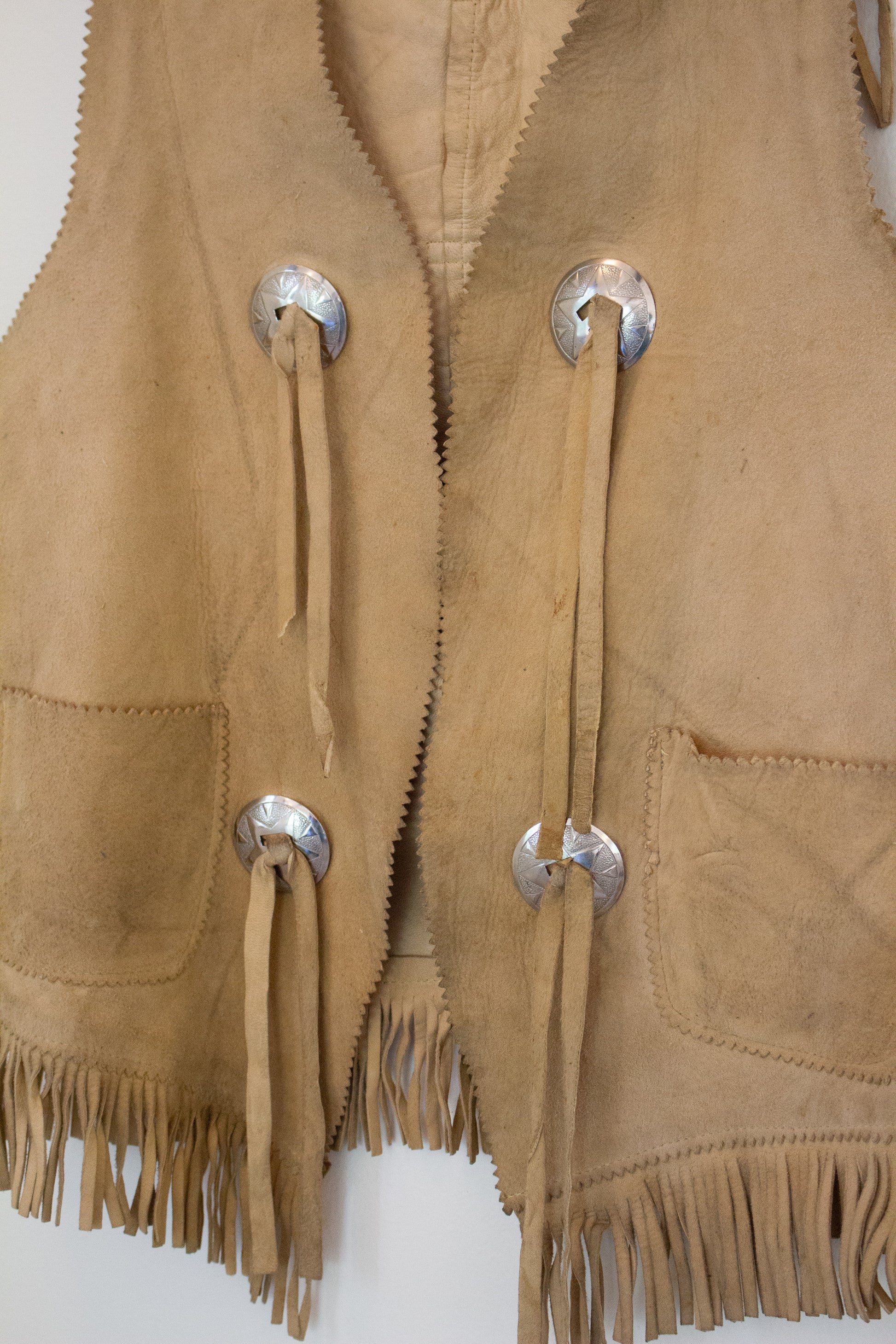Close up view of front of suede leather vest with silver buttons and tassels