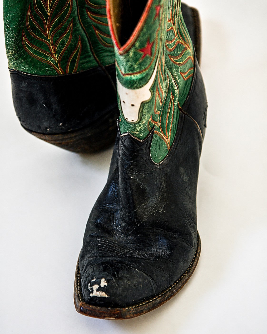 Black and green two-tone cowboy boots with longhorn and star inlay with scuff mark on toe