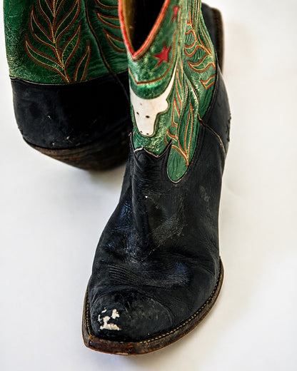 Black and green two-tone cowboy boots with longhorn and star inlay with scuff mark on toe