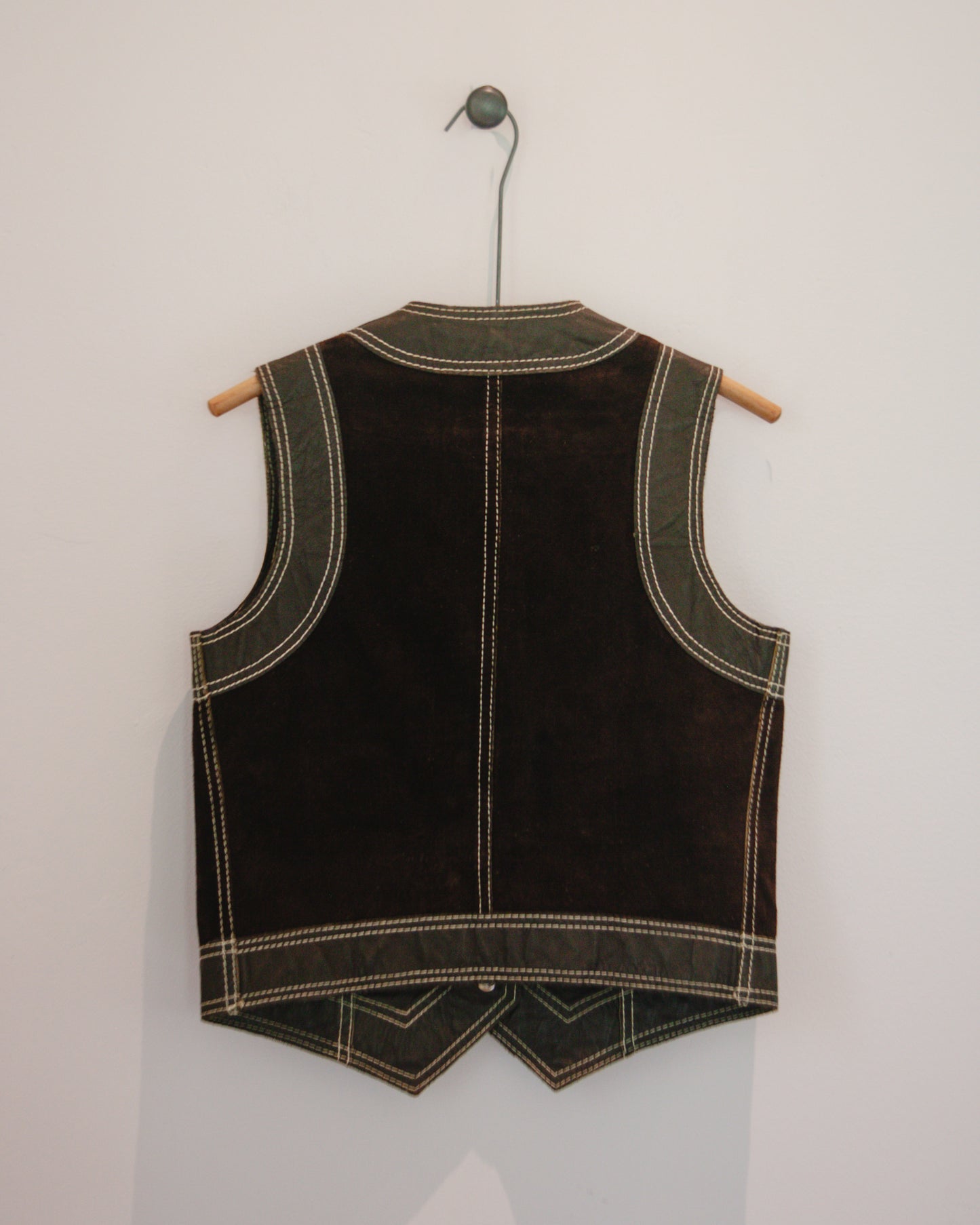 Back view of brown leather vest on a hanger against a white wall