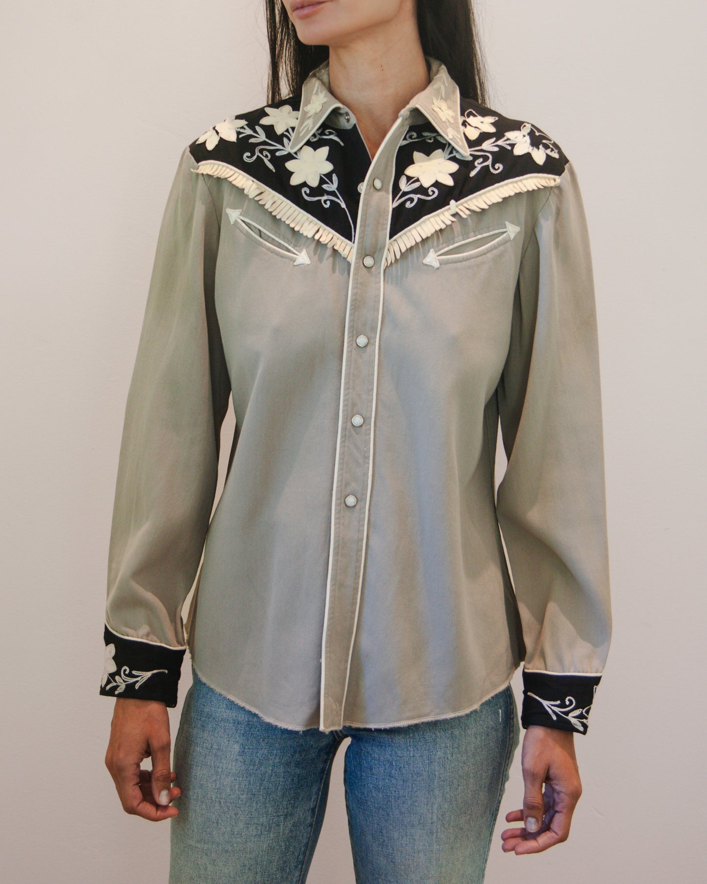 Light gray blouse with black and white embroidery worn by a person on a plain background
