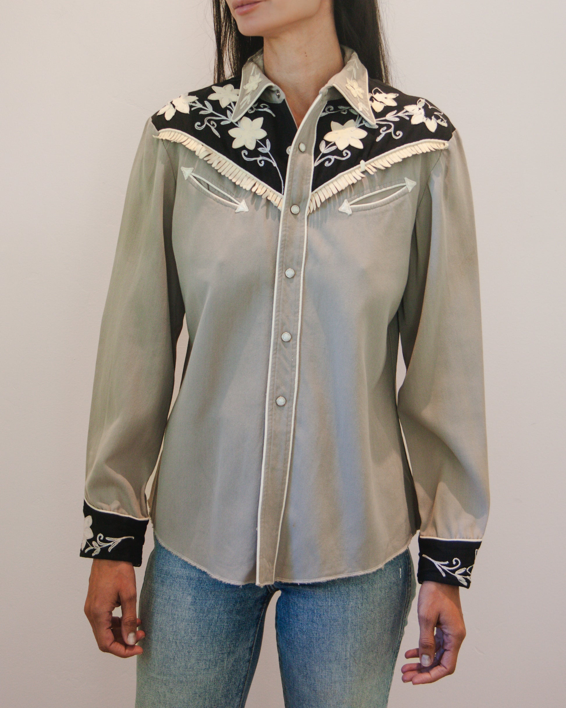 Light gray blouse with black and white embroidery worn by a person on a plain background