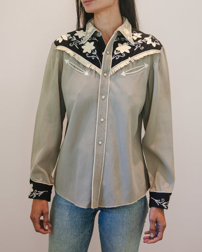 Light gray blouse with black and white embroidery worn by a person on a plain background