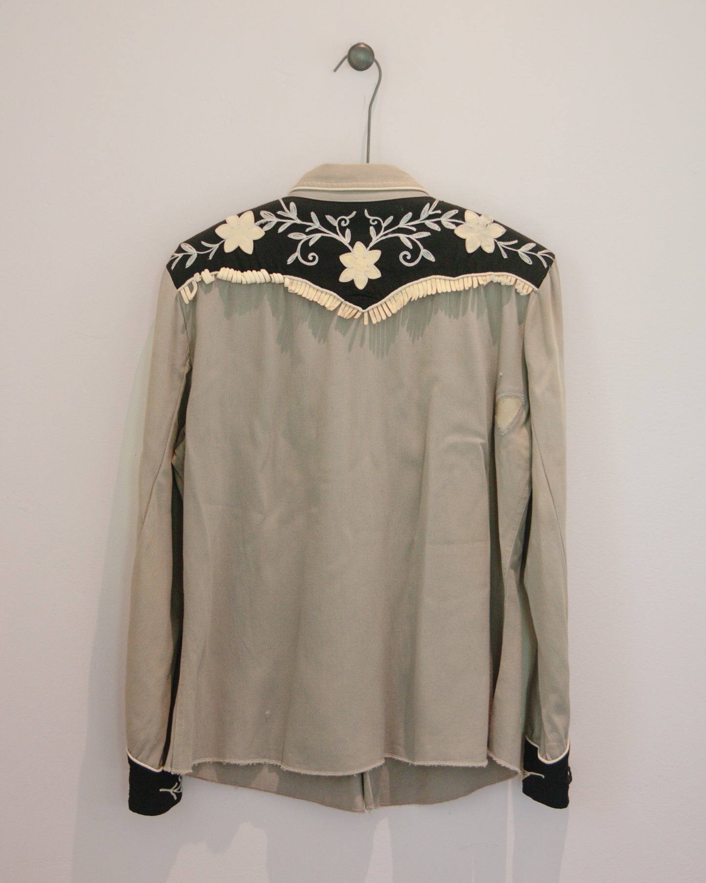 Gray blouse with floral embroidery on a hanger against a white background