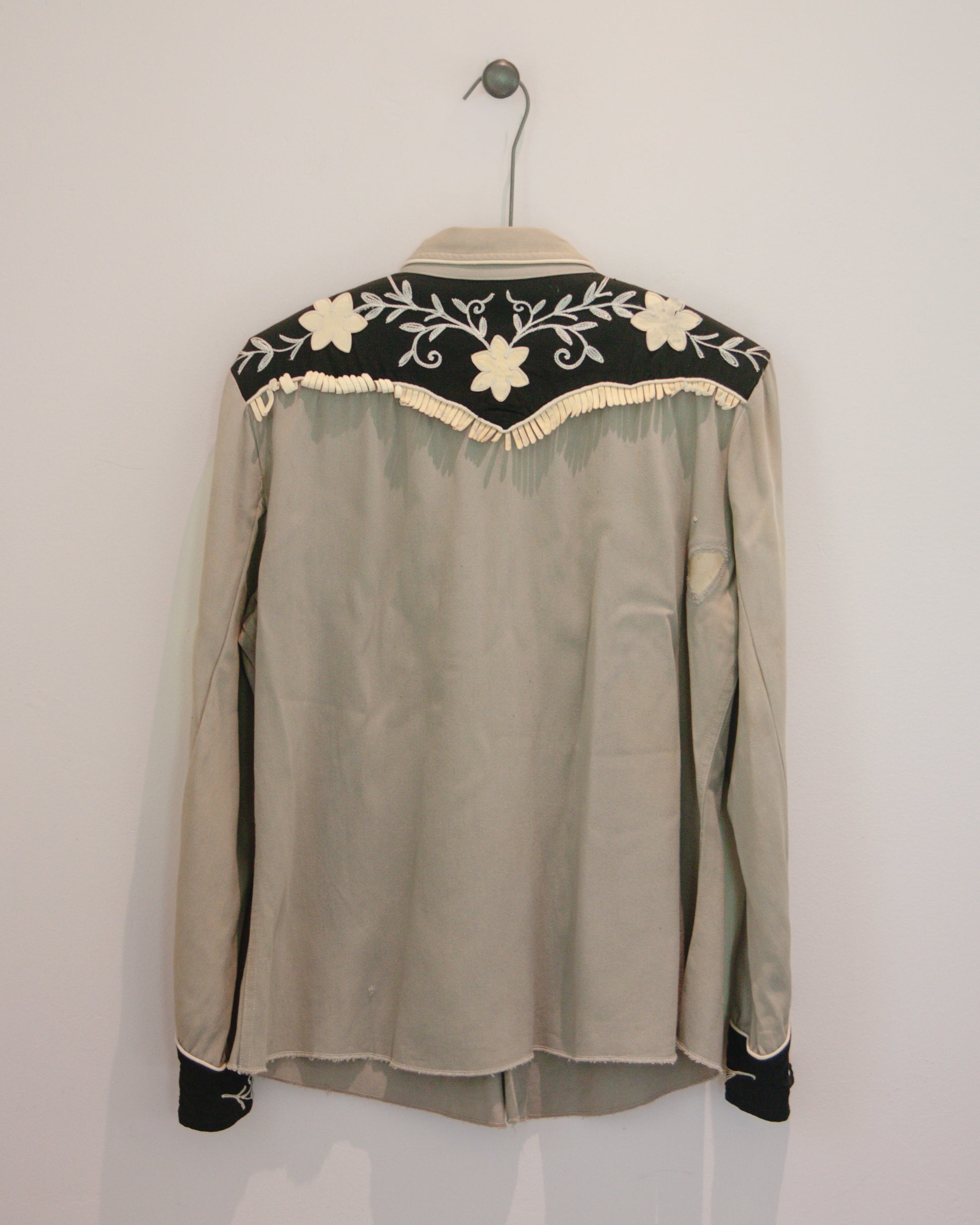 Gray blouse with floral embroidery on a hanger against a white background