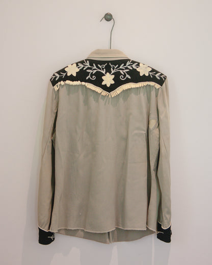 Gray blouse with floral embroidery on a hanger against a white background