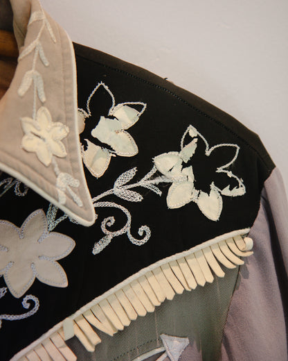 Embroidered black fabric with white floral patterns and fringe details.