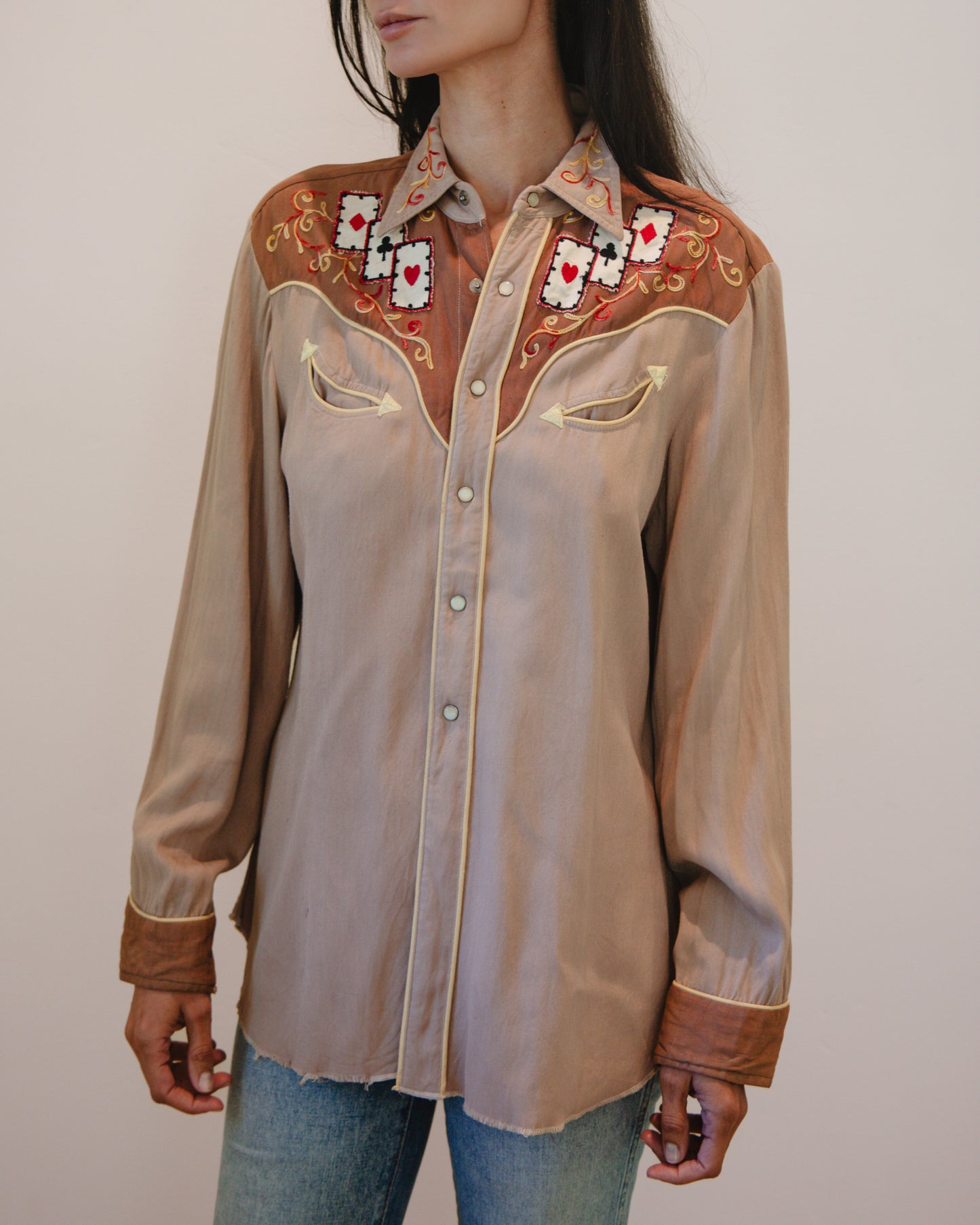 Beige embroidered shirt with card suits designs on a plain background