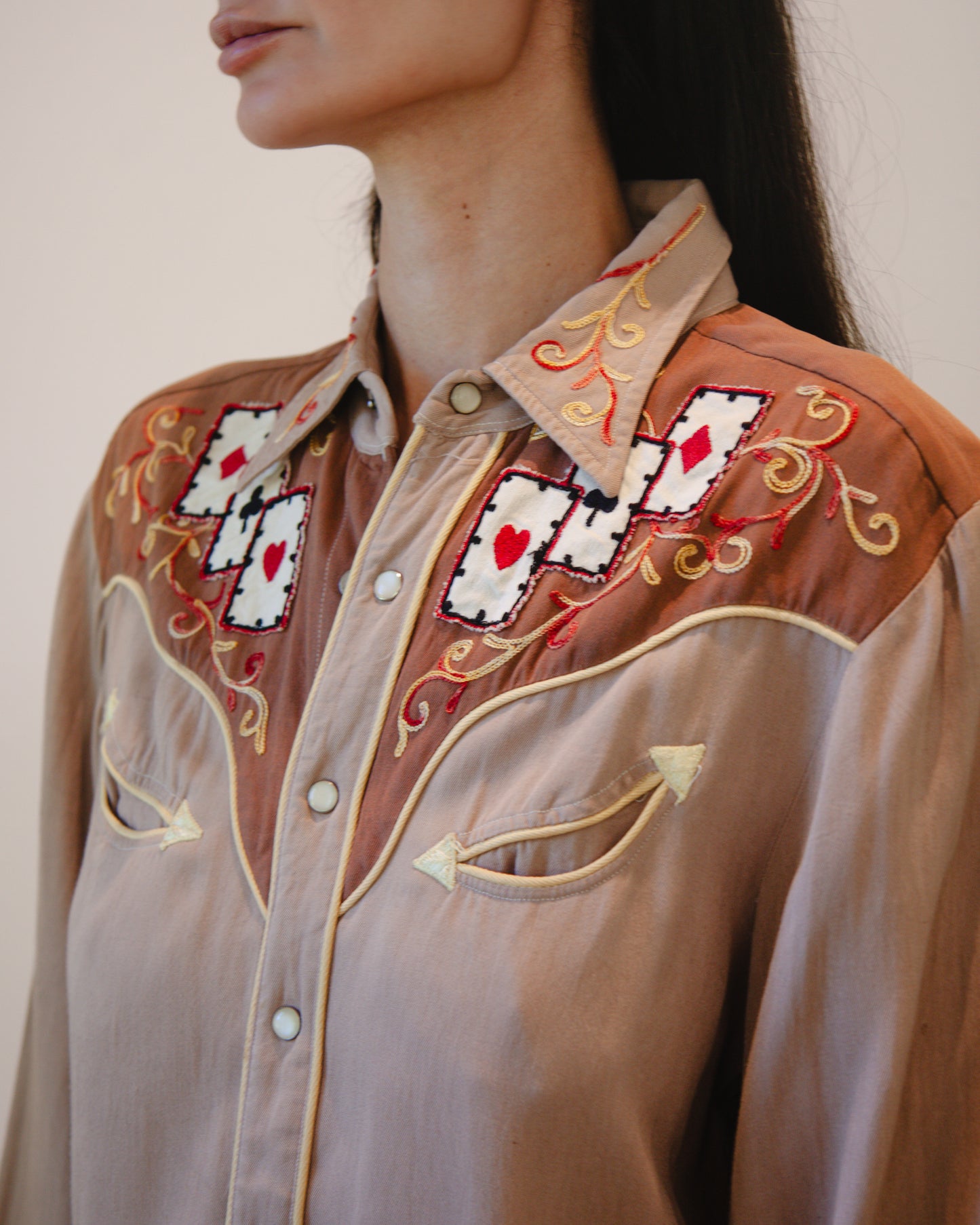 Close-up of a person wearing a brown embroidered shirt with card suits design.