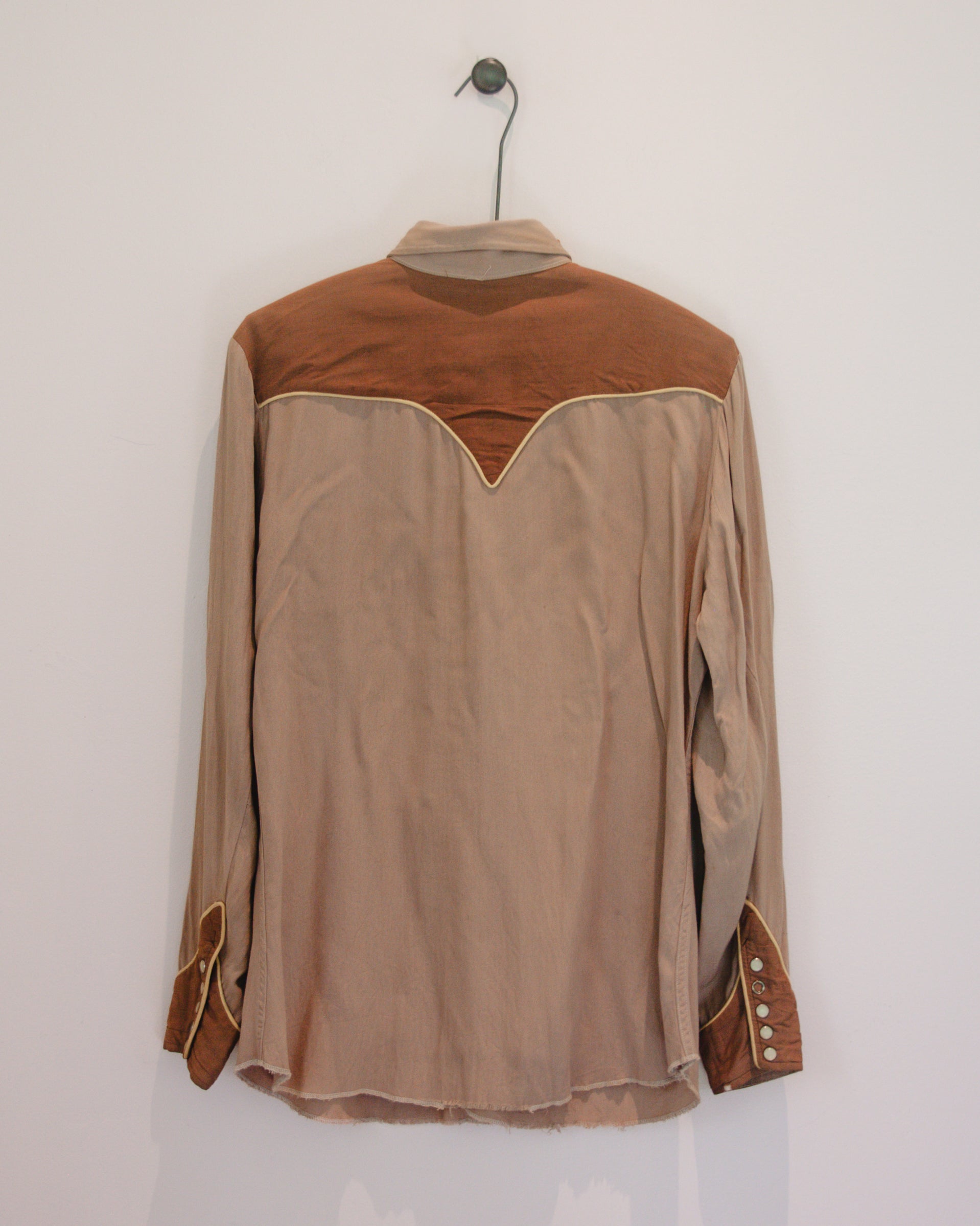 Brown and beige long-sleeve shirt on a hanger against a white wall