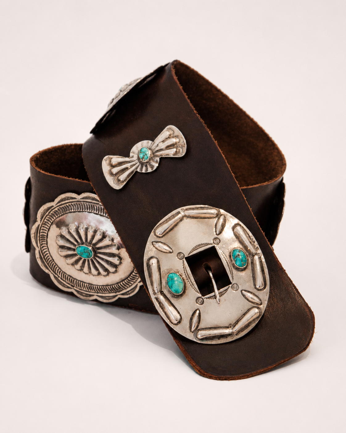 Brown leather belt with silver concho and turquoise stone design on a light gray background