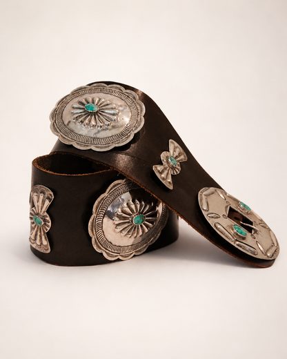 Brown leather belt with silver concho-style fastenings on a beige background