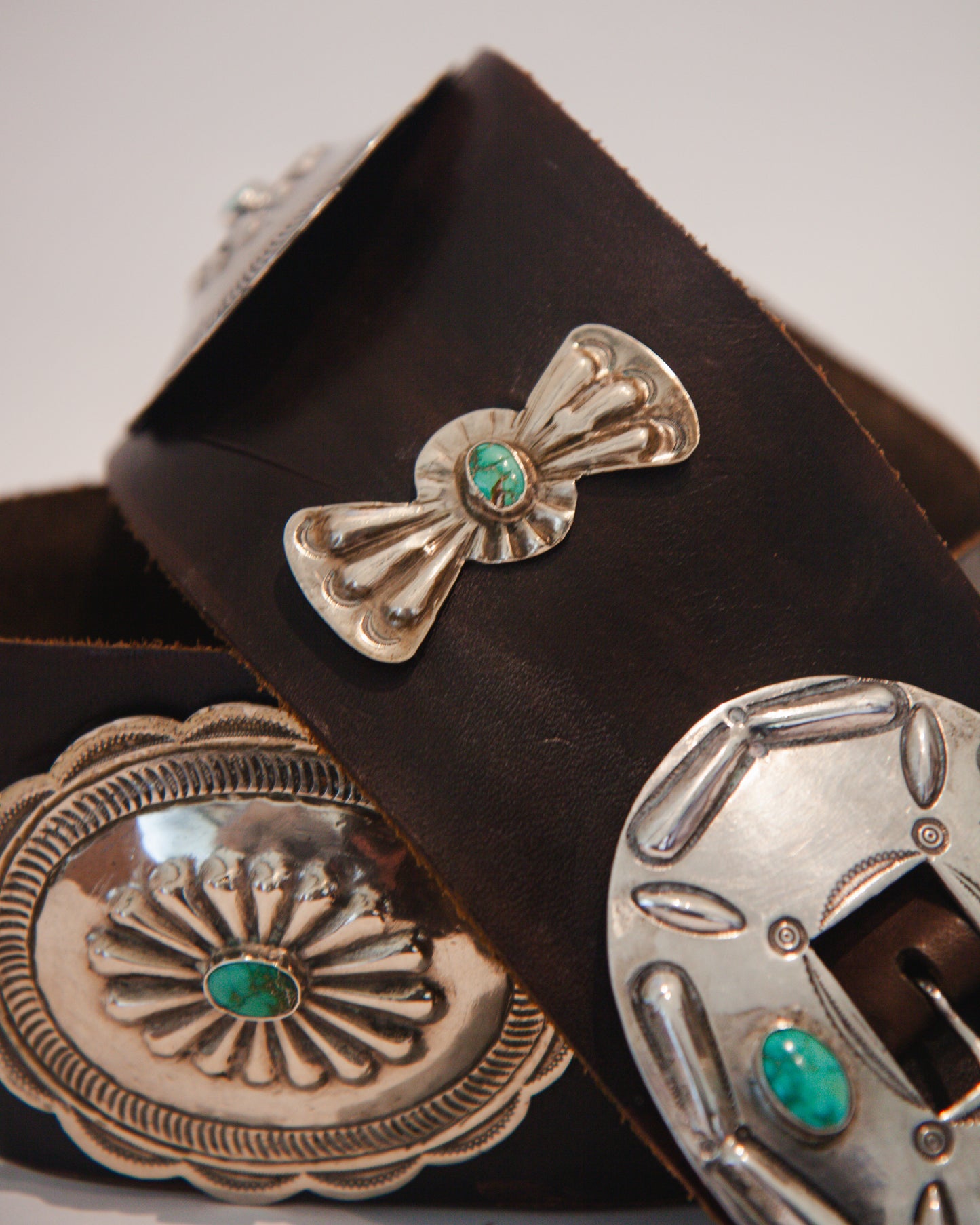 Close-up of silver concho belt with turquoise stones on a brown leather belt.