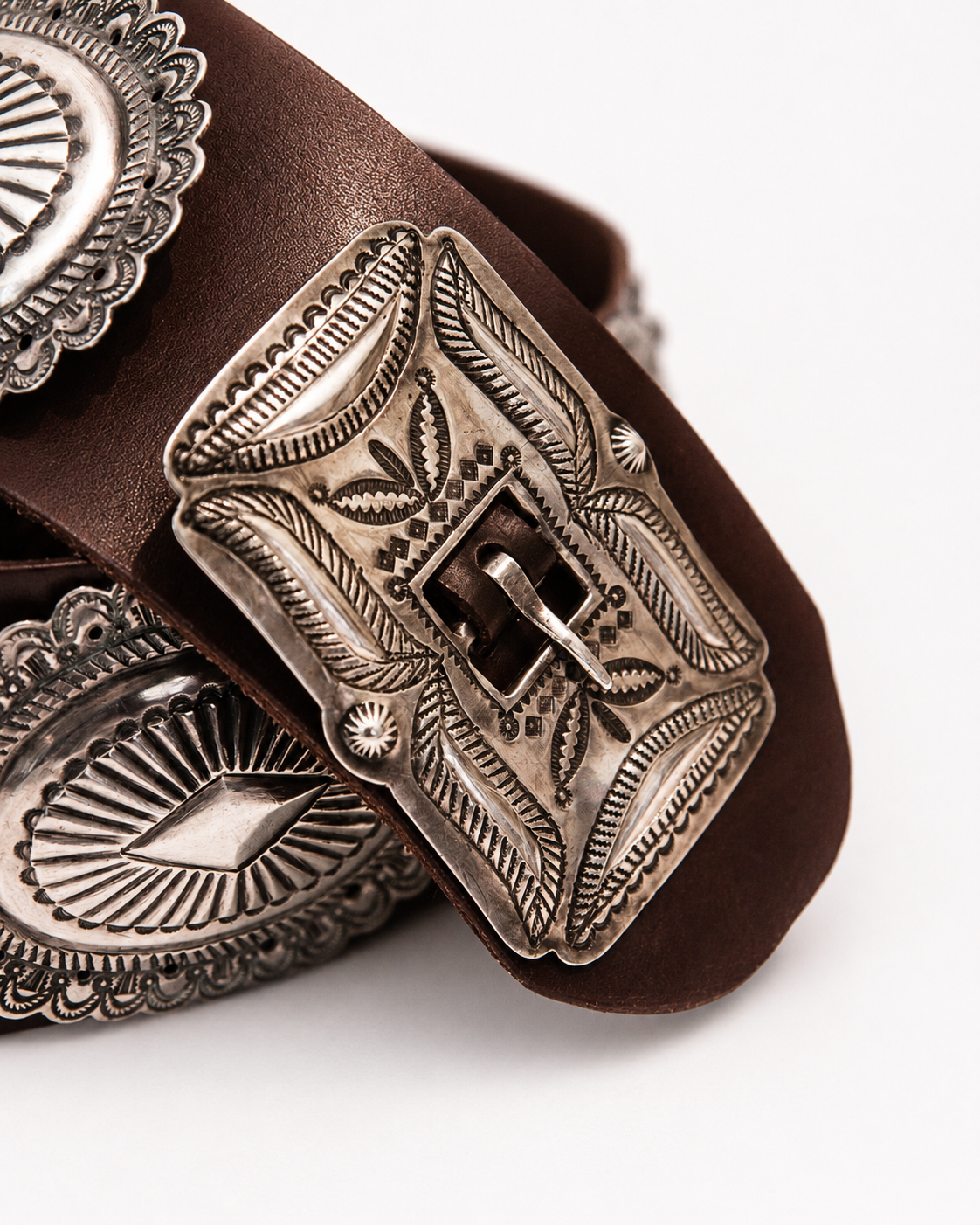 Close-up of a brown leather belt with an ornate silver buckle on a white background