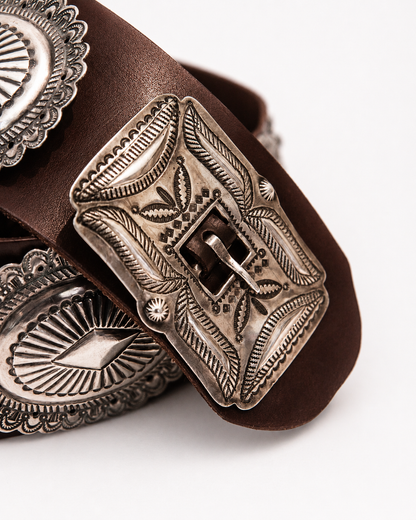 Close-up of a brown leather belt with an ornate silver buckle on a white background