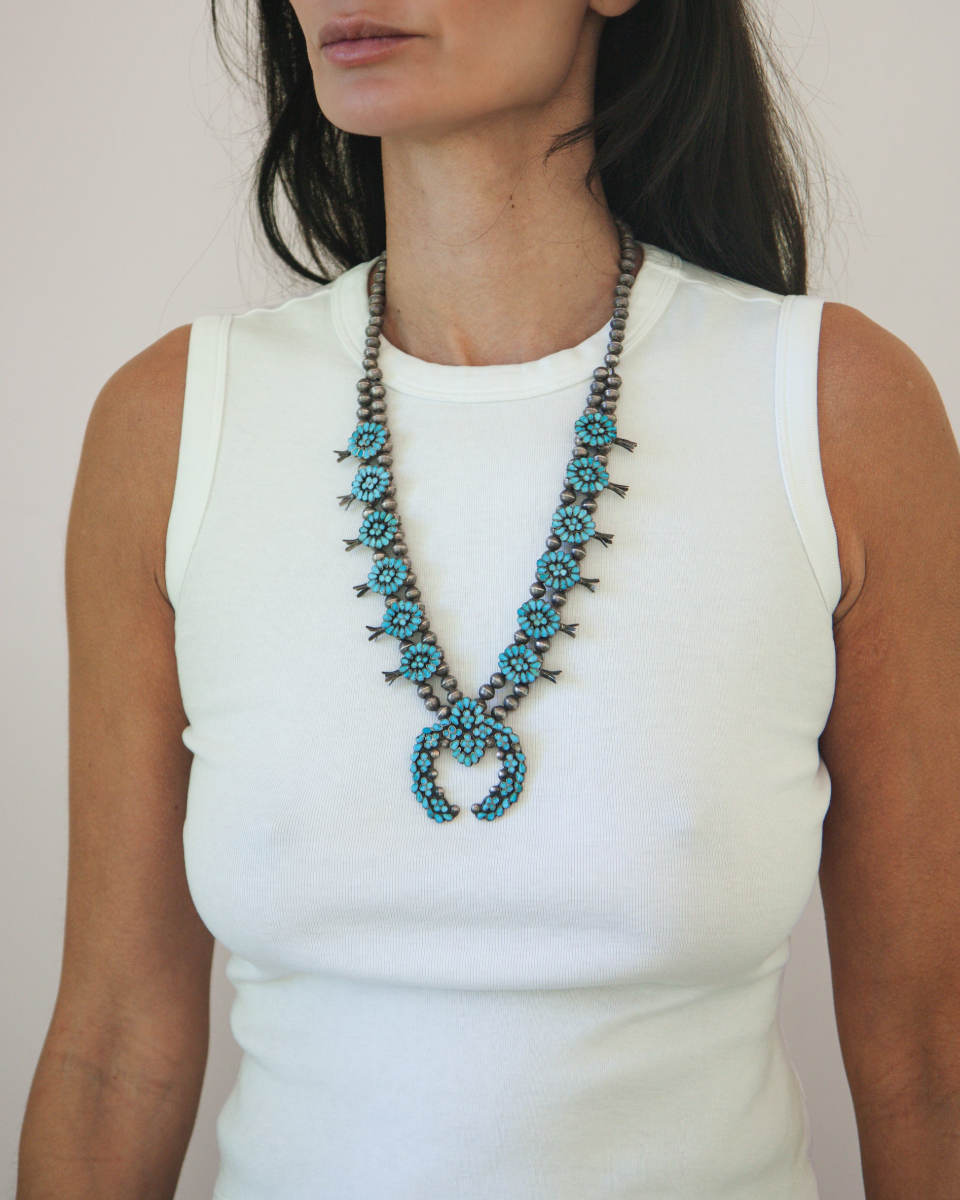 Woman wearing a long, beaded necklace with turquoise stones on a plain background