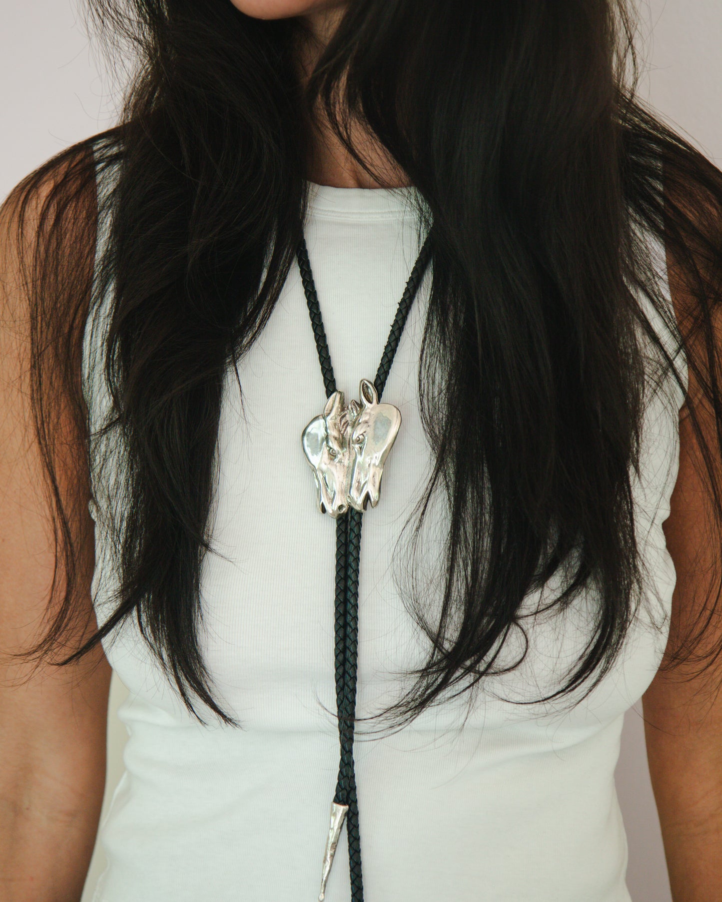 Person wearing a horse head bolo tie on a plain background