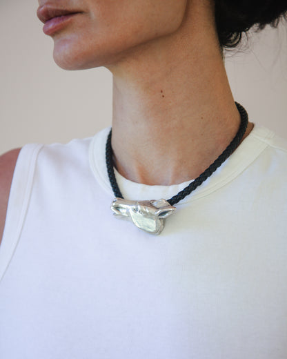 Person wearing a necklace with a silver horse pendant on a plain background