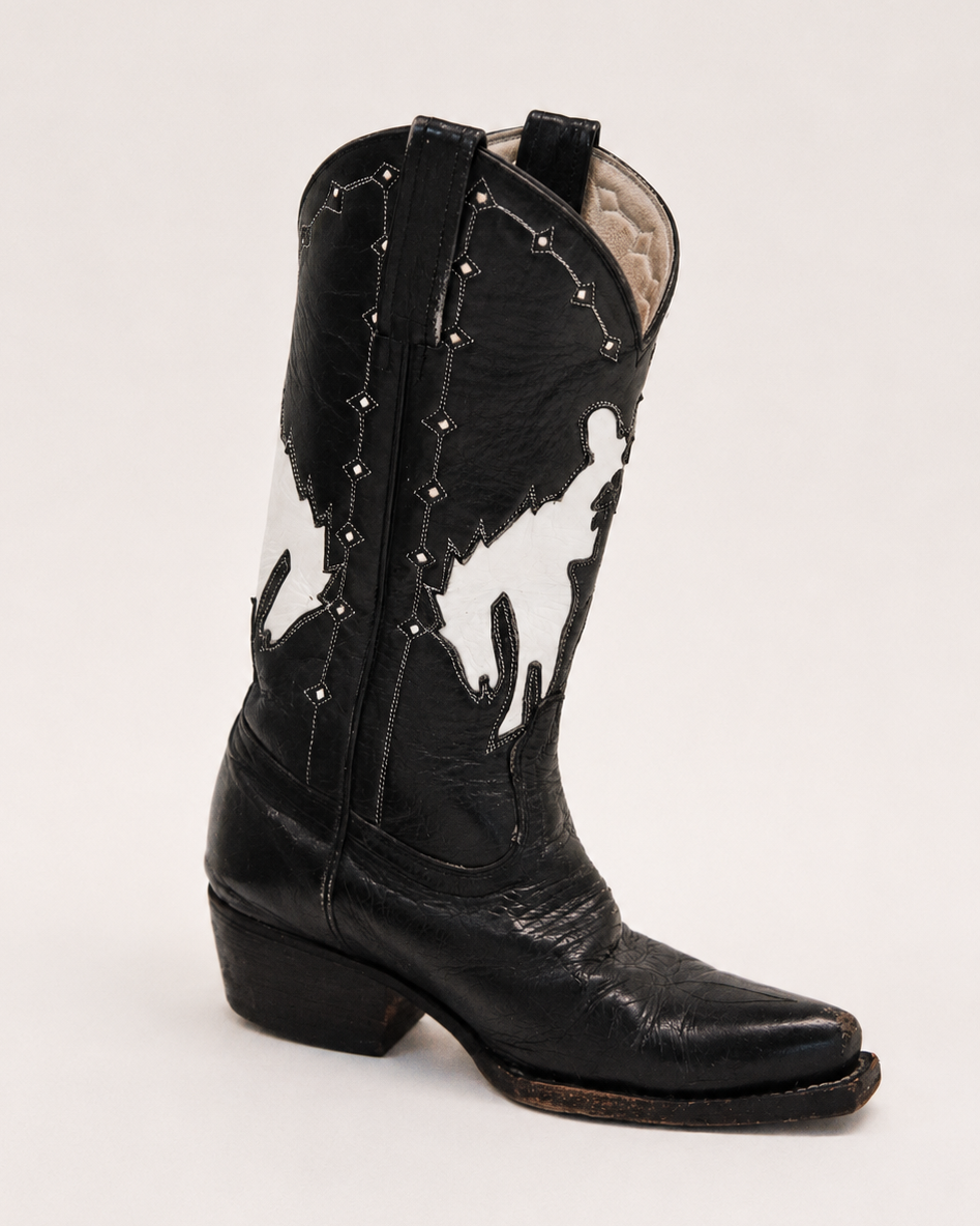 Black and white cowhide cowboy boot with studded details on a light gray background