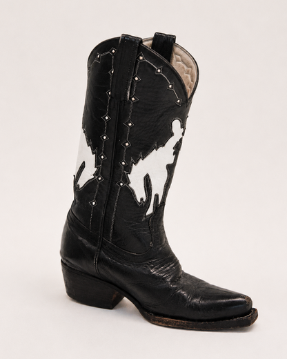 Black and white cowhide cowboy boot with studded details on a light gray background