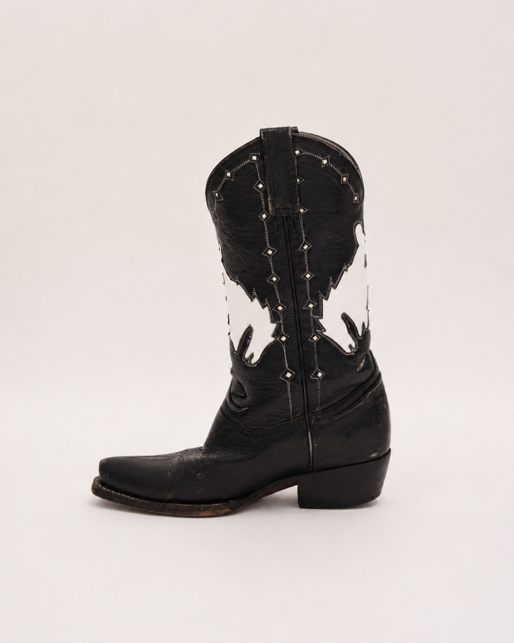 Black cowboy boot with white bucking bronco pattern on a light gray background