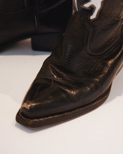 Close-up of a worn black leather cowboy boot toe on a white background