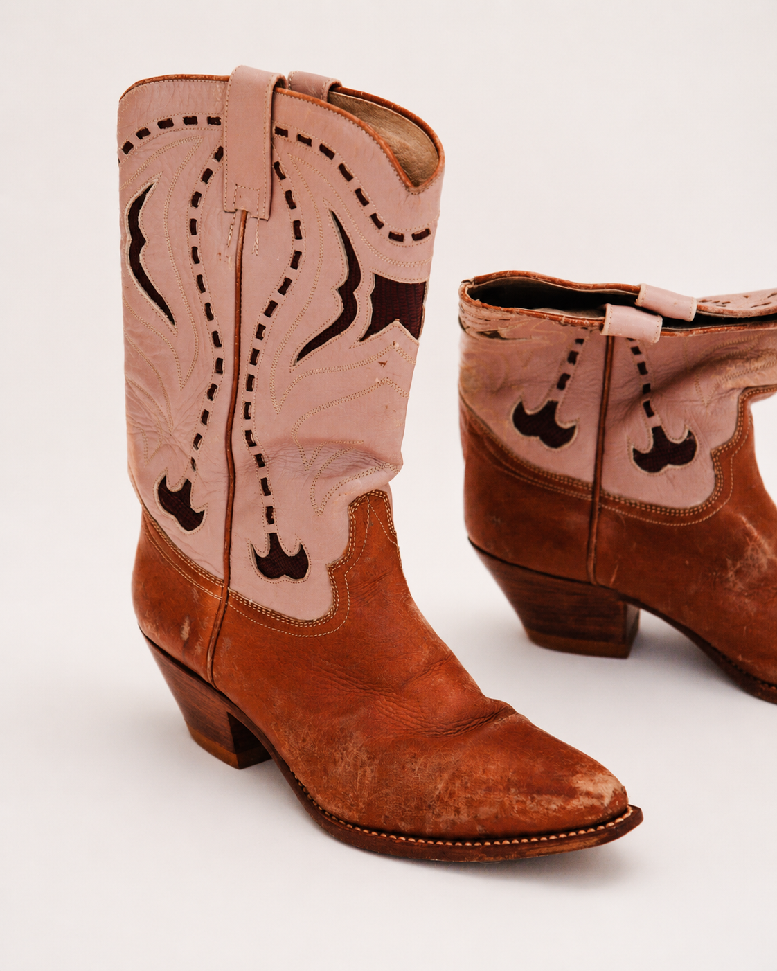 Pair of brown and pink cowboy boots with decorative patterns on a white background