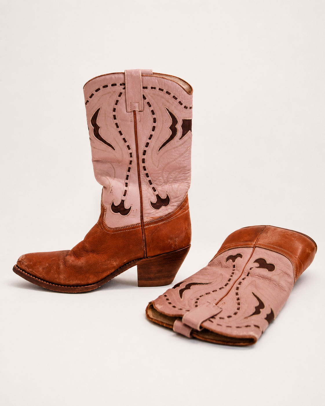 Pair of cowboy boots with pink uppers and brown soles on a light background