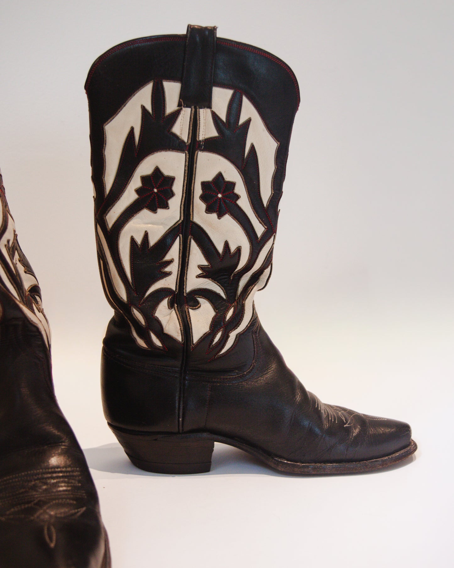 Black cowboy boot with white floral patterns on a white background
