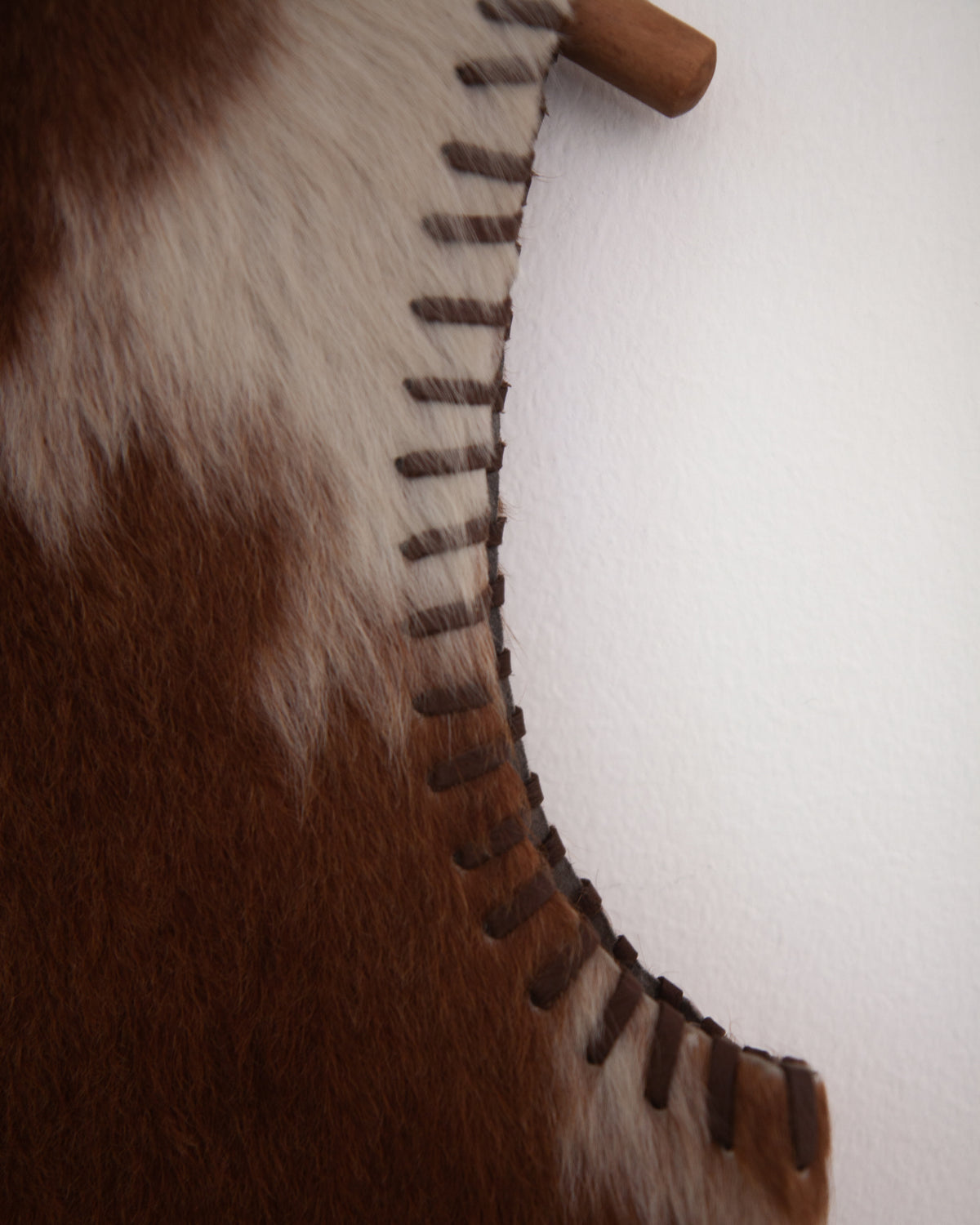 A brown faux fur vest with cowhide accents and whipstitching, detailed view on white background.