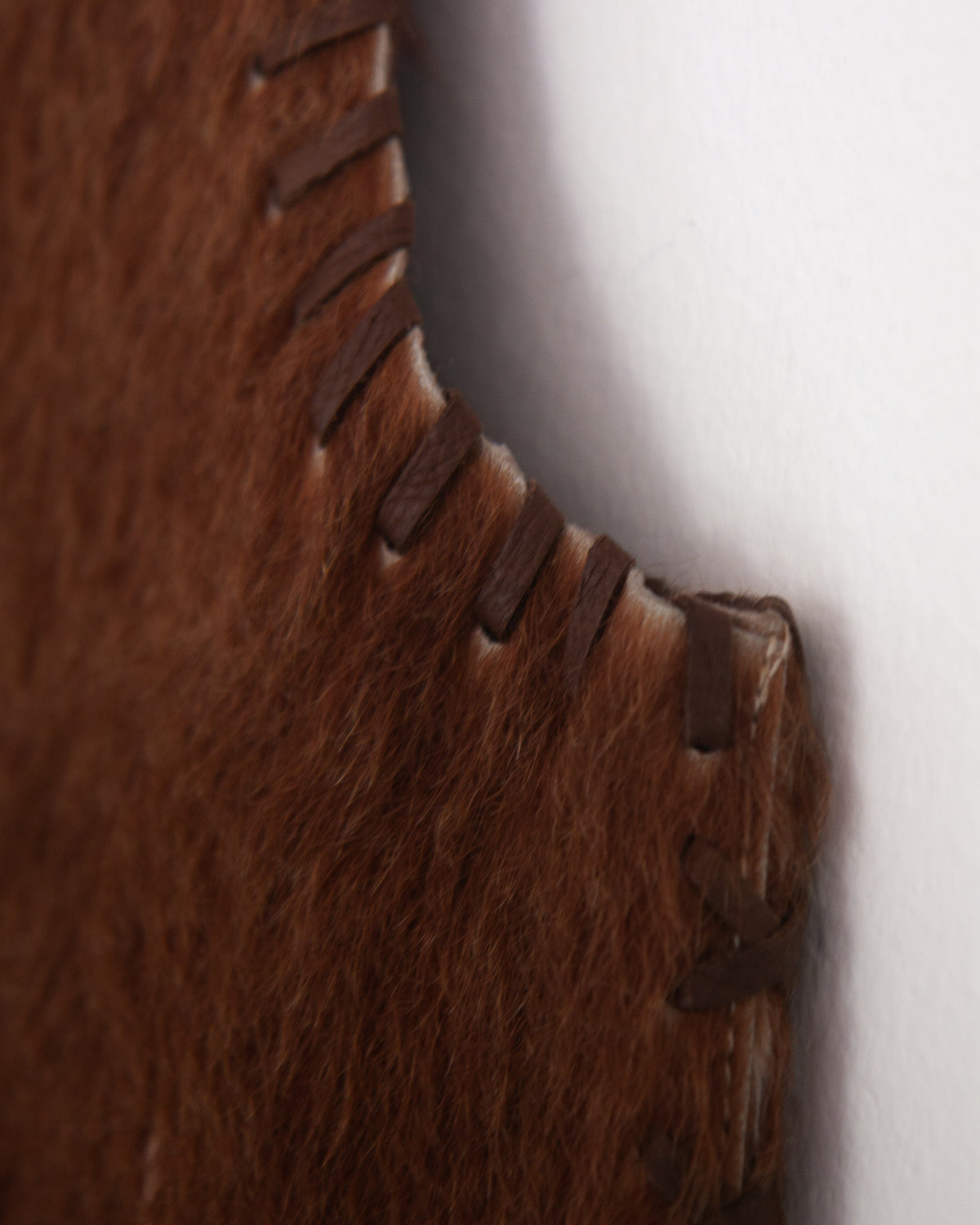 A brown faux fur vest with cowhide accents and whipstitching, detailed view on white background.