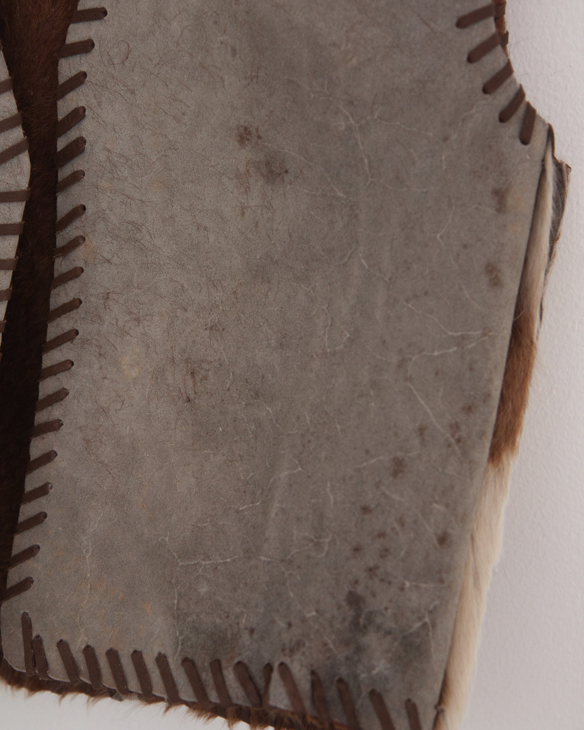 A close-up of a natural hide or leather panel with dark brown stitched edges and a textured, speckled surface.