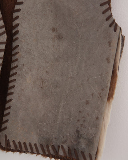 A close-up of a natural hide or leather panel with dark brown stitched edges and a textured, speckled surface.