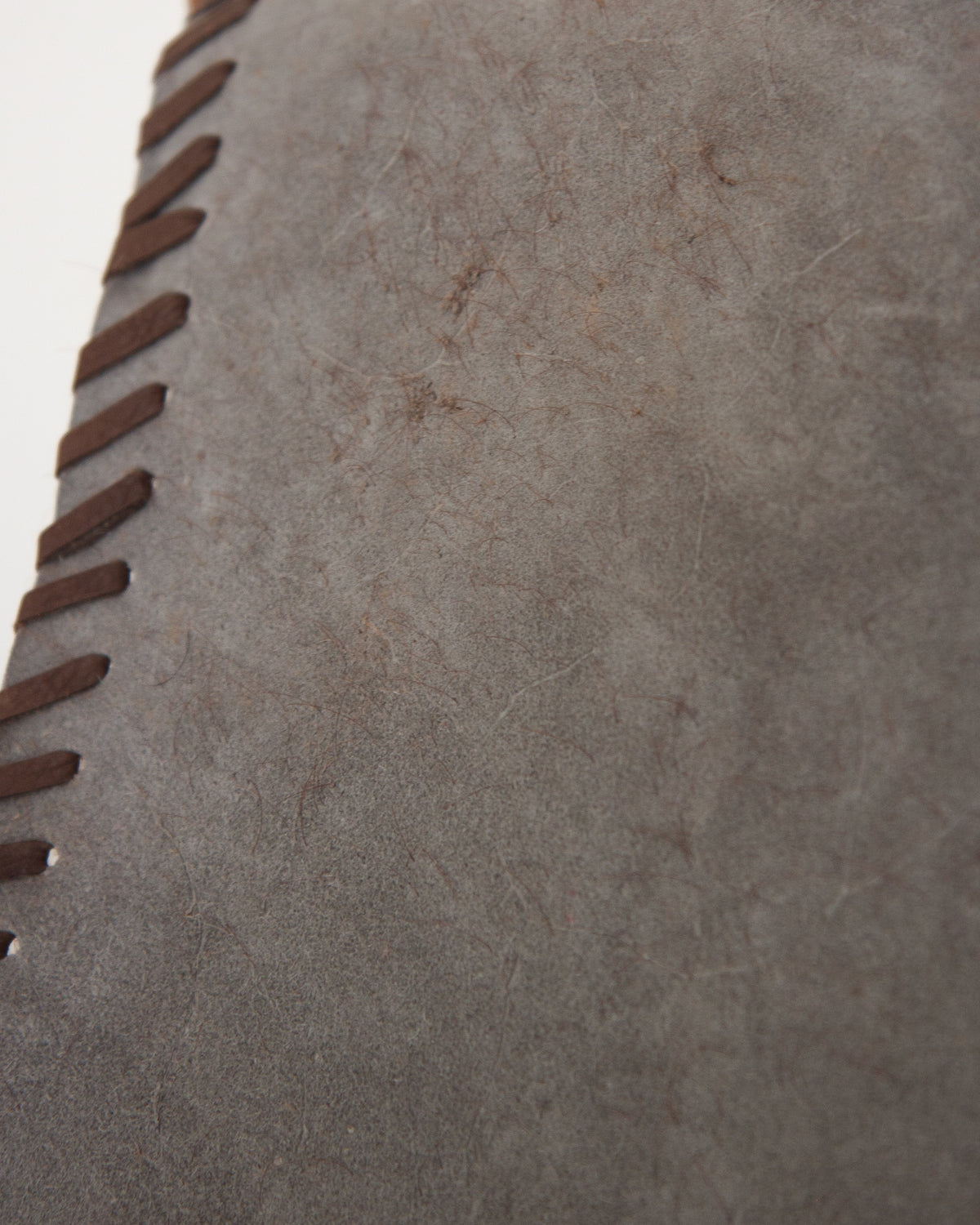 Close-up of a textured gray suede or leather surface with dark brown whipstitching along the left edge.