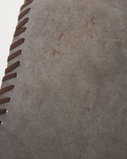 Close-up of a textured gray suede or leather surface with dark brown whipstitching along the left edge.