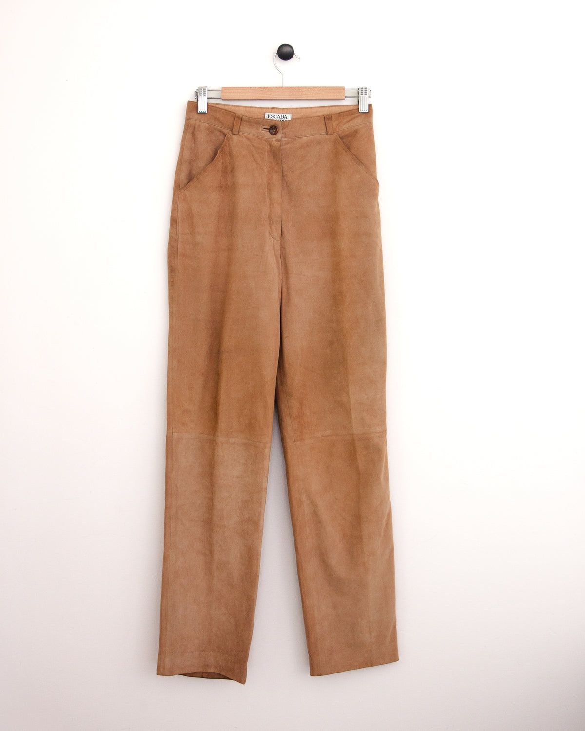 High-waisted tan corduroy trousers, a blue patterned button-up shirt, and brown suede shoes, standing against a plain off-white wall.