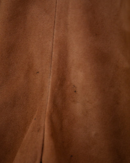 A close-up of a brown suede or suede-like fabric surface with a vertical seam and a few small dark specks.